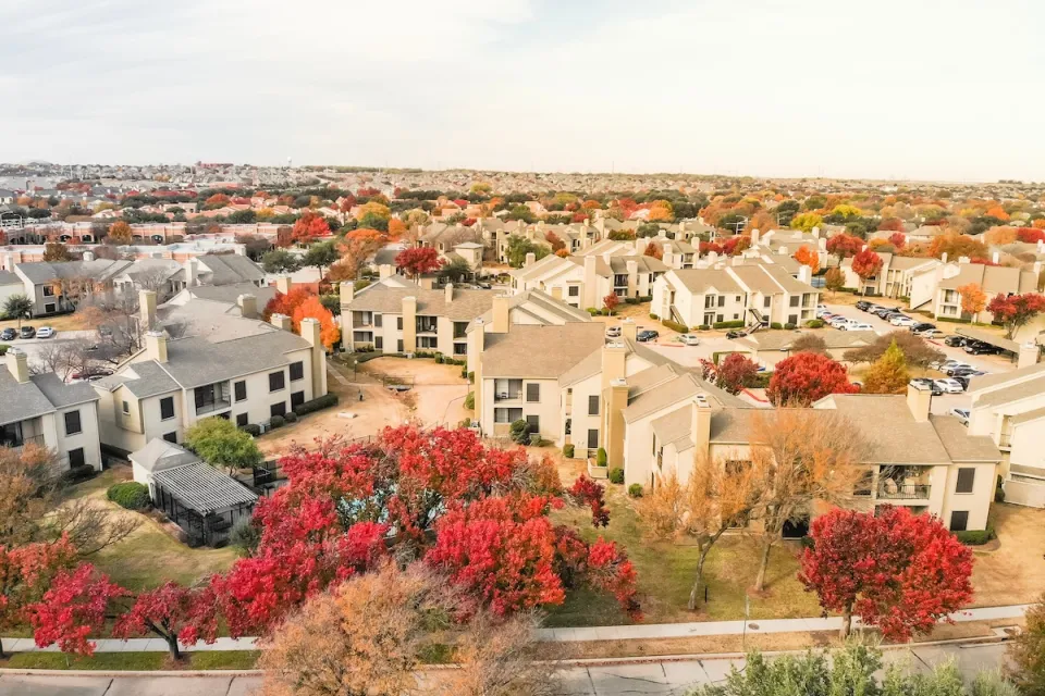 Aerial view of large complex of apartment buildings surrounded by fall foliage trees in suburban Dallas, Texas.